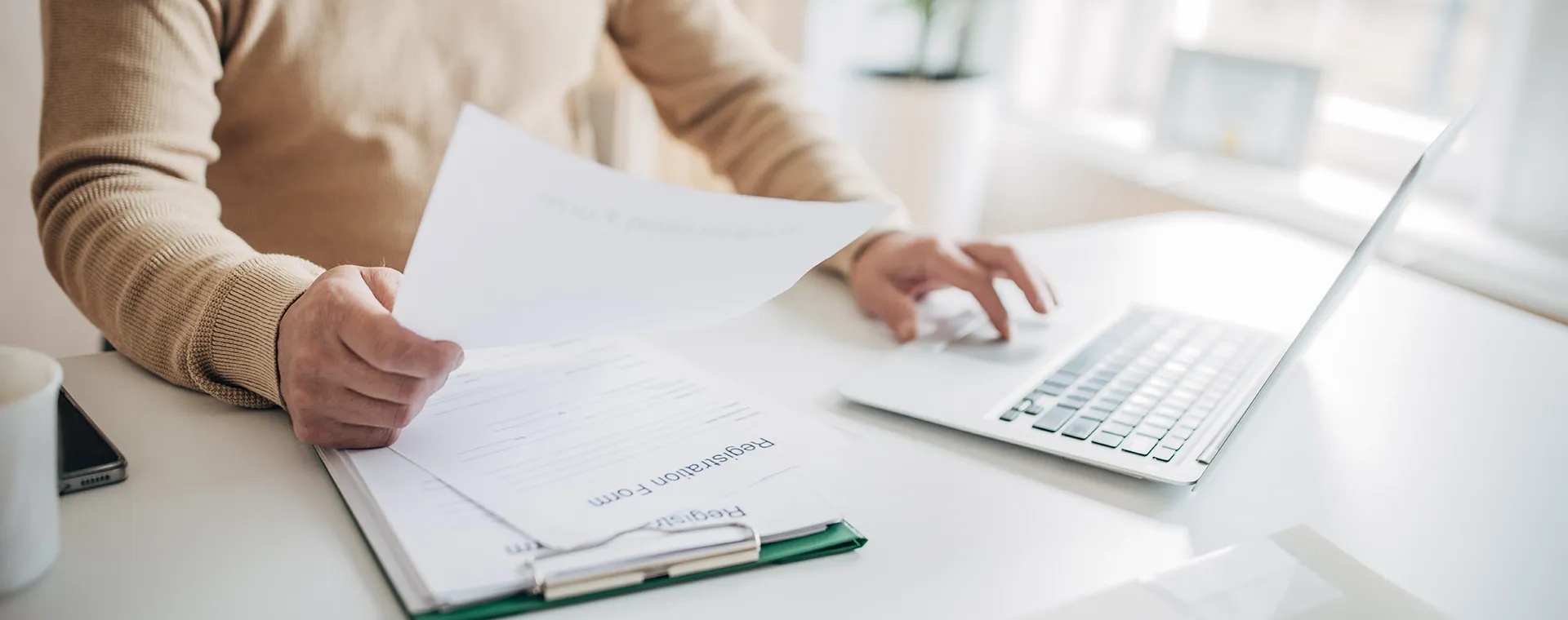 Individual interacting with papers and a laptop on a desk