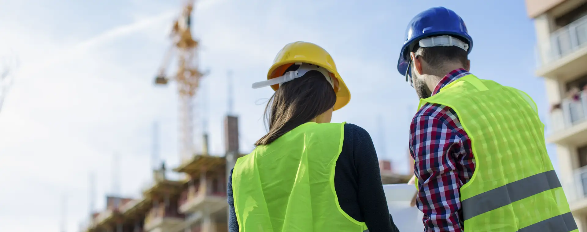 Two People in hi-vis looking at notes with a building under construction in the background