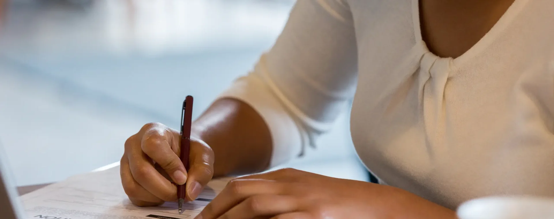 An Individual writing on a piece of paper on a desk in front of a laptop
