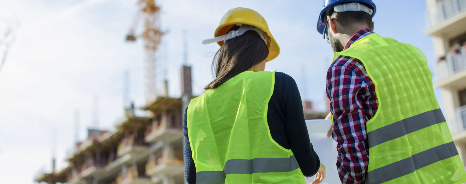 Two People in hi-vis looking at notes with a building under construction in the background
