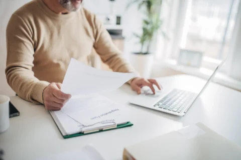 Individual interacting with papers and a laptop on a desk