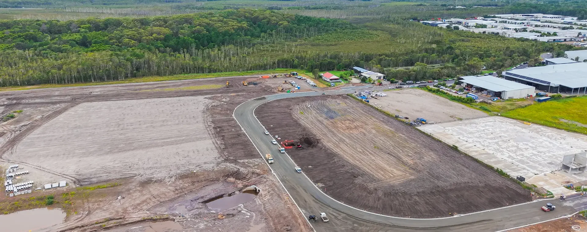 Aerial view of industrial development site in Coolum, showing earthworks, a newly formed road, and construction vehicles, with bushland nearby.