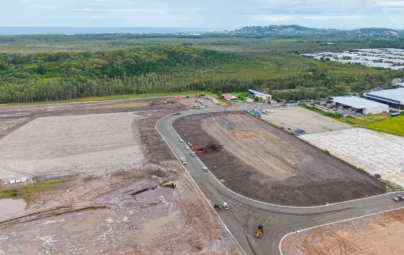 Aerial view of industrial development site in Coolum, showing earthworks, a newly formed road, and construction vehicles, with bushland nearby.